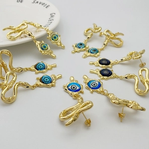 Macro detail of golden snake earrings with blue evil eye charms on a white background