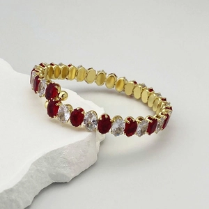 Détail d'un bracelet élastique doré avec cristaux ovales rouges et blancs sur pierre