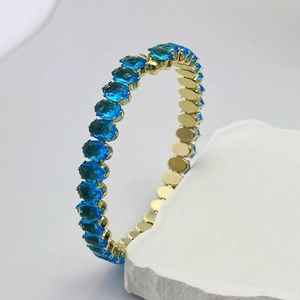 Détail d'un bracelet doré orné de zircons bleus ovales sur support en pierre