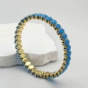Gros plan d'un bracelet doré avec zircons bleu ciel sur une pierre de marbre blanc
