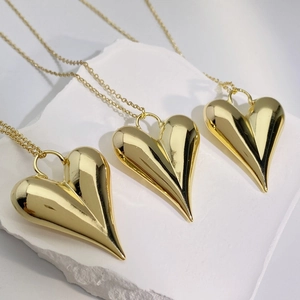 Detailed macro shot of three 18K gold plated heart pendants on a textured stone platform