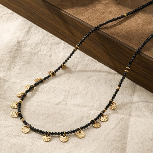 Dettaglio della collana lunga con pietre nere sfaccettate e pendenti dorati con texture