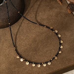 Dettaglio di collana vintage con perle nere sfaccettate e pendenti in oro martellato