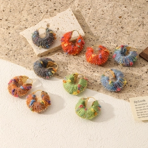 Close-up of handmade rainbow wool wrapped earrings with gold bead accents on retro props