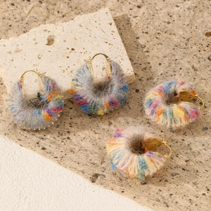 Detailed view of handmade colorful yarn-wrapped gold hoop earrings on natural stone