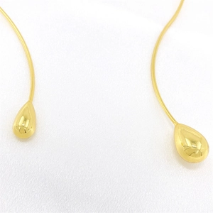 Macro detail of polished gold teardrop charms on a minimalist metal neck torque