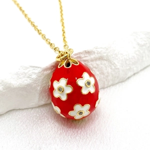 Detailed macro of a 14K gold-plated red enamel egg pendant with white flower crystal inlays