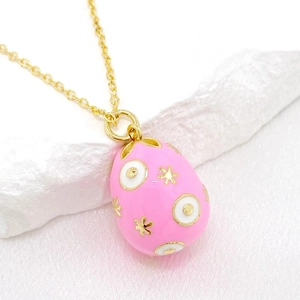 Macro shot of pink enamel egg pendant with gold stars and white dots on silk background
