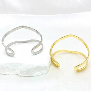 Minimalist silver and gold woven open cuff bracelets on white textured stone background