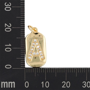 Dettaglio del ciondolo ovale dorato con lettera A in zircone accanto a un righello