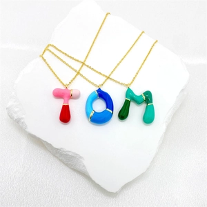 Detailed close-up of three gold necklaces with colorful puffy enamel letter pendants spelling TOM