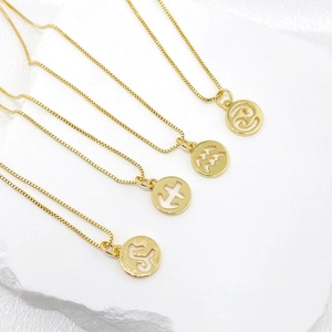 Close-up of four gold zodiac pendants with hollow astrological symbols on box chains