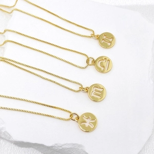 Detailed view of gold zodiac sign pendants on fine box chains over white marble texture