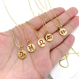 Macro shot of gold zodiac pendant necklaces held in hand, showing Capricorn and Leo signs