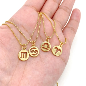 Detail view of four gold zodiac coin necklaces held in palm showing scale and texture