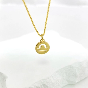 Macro shot of gold Libra zodiac pendant with minimalist cutout design on marble