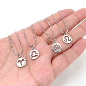 Detailed view of silver zodiac pendants on hand featuring Aries, Libra, and Leo signs