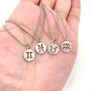 Macro shot of silver zodiac pendant necklaces in palm to show accurate product size and scale