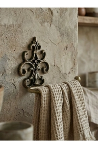 Detail of vintage cast iron fleur-de-lis towel holder with bronze finish on stone wall
