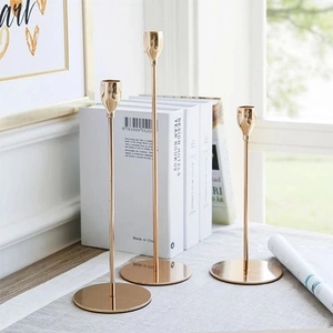 Set of three gold pillar metal candle holders with mirror polished finish on gray tabletop