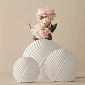 Three-piece white ceramic vase set with leaf texture and pink flowers in home setting