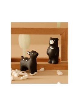 Detail of matte black ceramic animal figurines featuring a deer and bear on pebbles