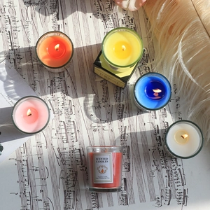 Set bunte Duftkerzen im Glas auf Notenblättern mit Federn für die Dekoration