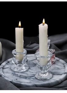Detail view of transparent glass candle holders on marble tray with warm candle flame