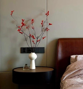 Minimalistische weiße Keramikvase mit roten Blumen auf einem schwarzen Nachttisch im Schlafzimmer