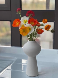 Detail einer weißen matten Keramikvase mit gerippter Textur und bunten Mohnblumen im Inneren