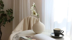 Close-up of minimalist off-white ceramic vase with horizontal texture on marble table