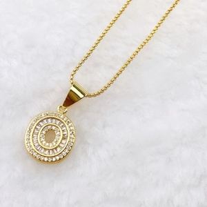 Close-up of golden letter O pendant with cubic zirconia on white plush background