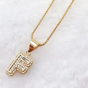 Close-up of gold letter F pendant with zirconia stones on a white plush background