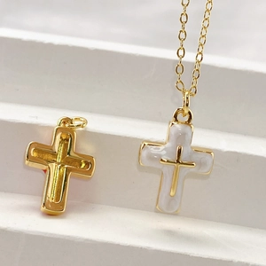 Golden cutout cross pendant and white enamel cross necklace on a white tiered stand