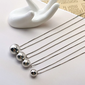 Detailed view of four different sized brushed silver sphere pendants on box chains
