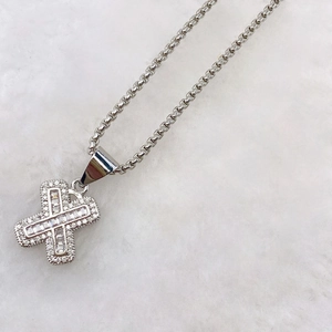 Macro detail of silver X-shaped pendant with cubic zirconia pave and box chain