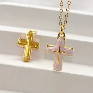 Macro shot of pink marble enamel cross pendant and gold metallic cross on white display