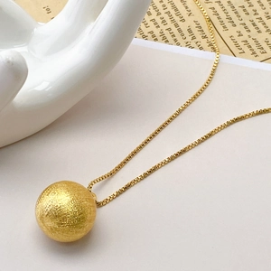 Macro view of a gold hollow ball pendant with a brushed matte texture on a box chain