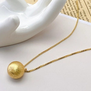 Detailed close-up of a golden box chain necklace with a matte frosted sphere pendant