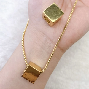 Polished gold cube pendant necklace with box chain on soft white plush background