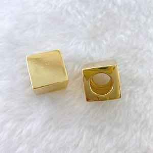 Macro view of polished gold plated cube spacer beads with hole on soft white fabric