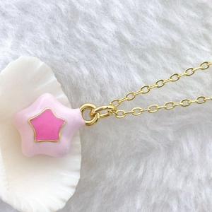Close-up of pink layered star pendant with gold trim on shell and plush background