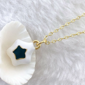 Detail of a white enamel star pendant with a blue center on a gold-plated link chain