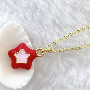 Detail shot of a double-layered red and pink star pendant on a gold cross chain
