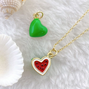 Detail of heart-shaped watermelon enamel pendant with gold loop on white faux fur background