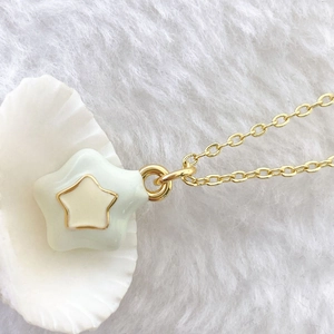 Close-up of gold chain necklace featuring a mint green enamel star pendant with gold trim