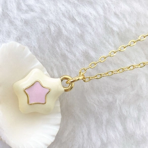 Macro detail of a gold-plated star pendant with creamy white and pink enamel finish