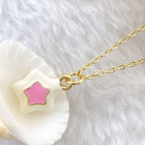 Macro shot of gold star necklace with white and pink enamel pendant on white fur background