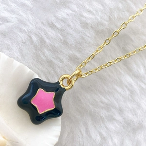 Close-up of a gold-plated star pendant with black and pink enamel on a white plush rug