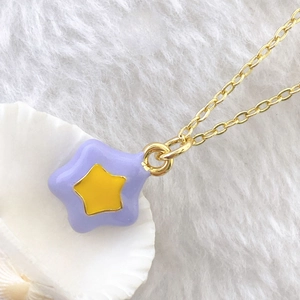Detailed macro view of purple enamel star pendant with gold chain on white fur